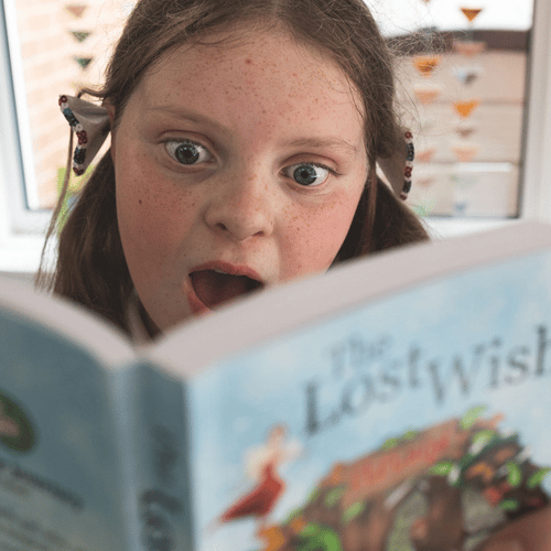 young girl looking shocked whilst reading a copy of the lost wish book