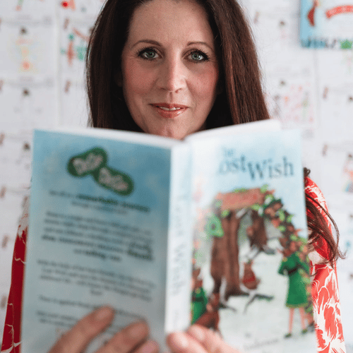 clare anderson smiling softly whilst holding open copy of the lost wish