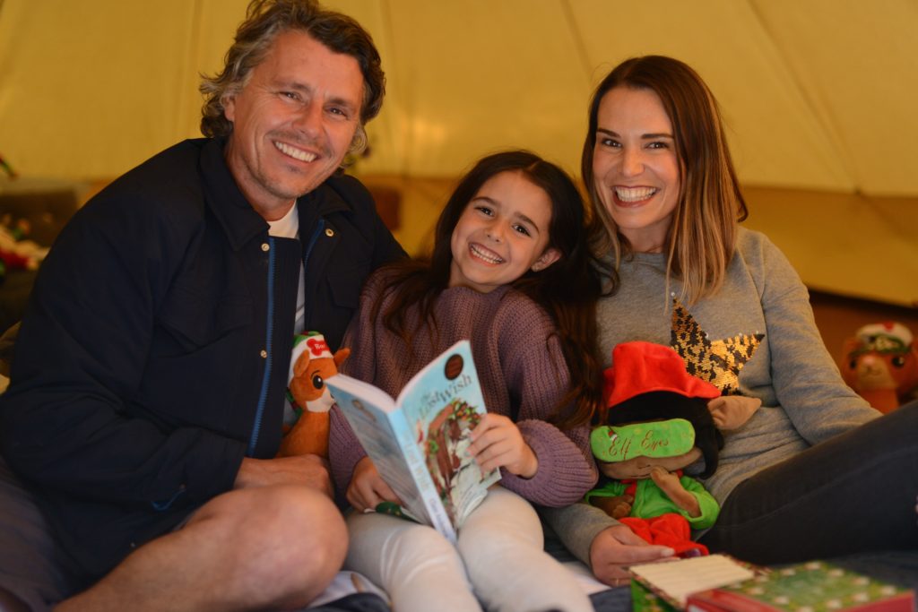 father, daughter and mother in a tent reading a book smiling at camera